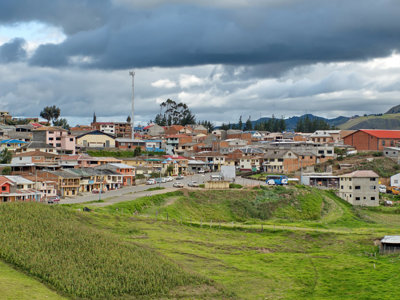 Dorp in de Ecuadoraanse Andes met kleurrijke huizen, groene velden en donkere wolken boven de heuvels.