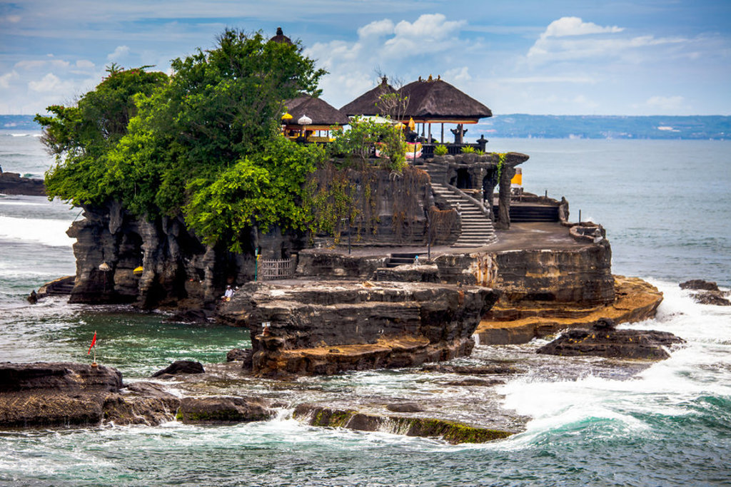 Tanah Lot-tempel op Bali, op een rots in zee met golven en groene begroeiing.