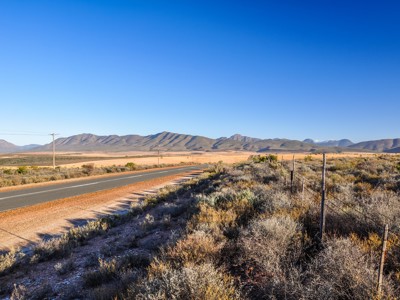 Lange weg door het Zuid-Afrikaanse Karoo-landschap met bergen onder een heldere blauwe lucht.