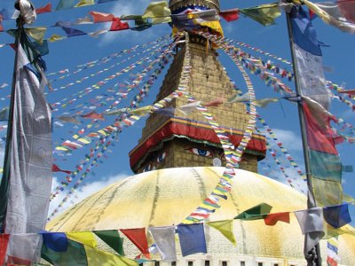 Boudhanath-stoepa in Kathmandu met gebedsvlaggen tegen een blauwe lucht.