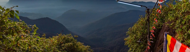 Zonsopkomst bij Adams Peak in Sri Lanka, met gebedsvlaggen langs het bergpad en uitzicht op mistige valleien.