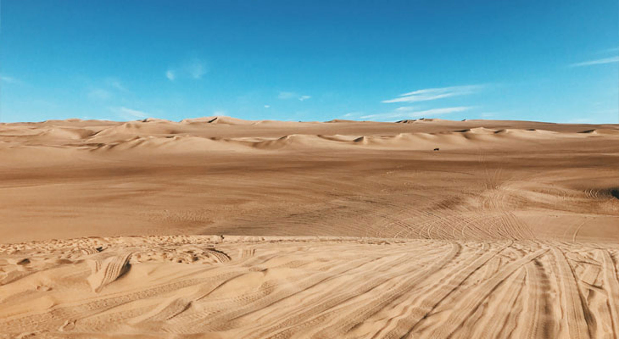 Zandduinen in de woestijn van Peru onder een helderblauwe lucht.