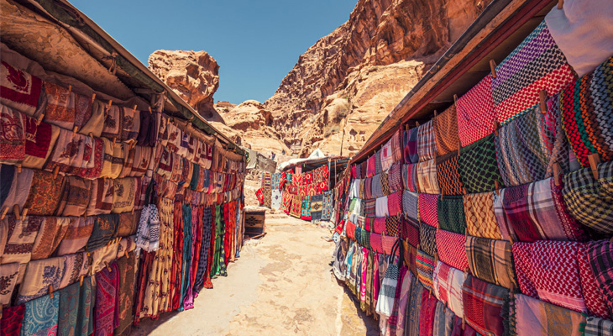 Souvenirmarkt met kleurrijke sjaals en doeken tussen de rotsen van Petra, Jordanië.