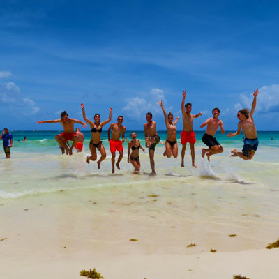 Gezin springt juichend in de lucht op een wit zandstrand in Mexico tijdens familiereis hoogtepunten.