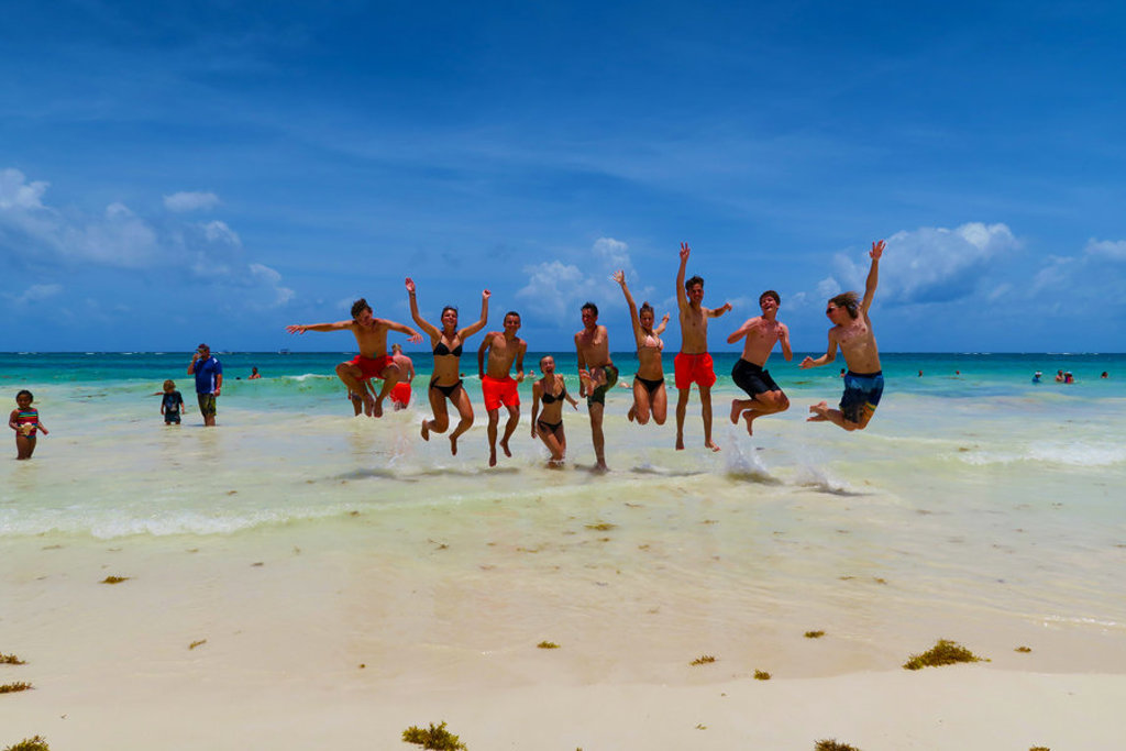 Gezin springt juichend in de lucht op een wit zandstrand in Mexico tijdens familiereis hoogtepunten.
