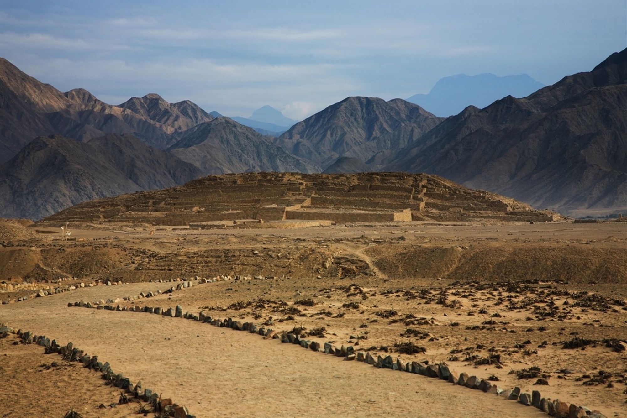 Ruïnes van de precolumbiaanse stad Caral in Peru, met bergen op de achtergrond.