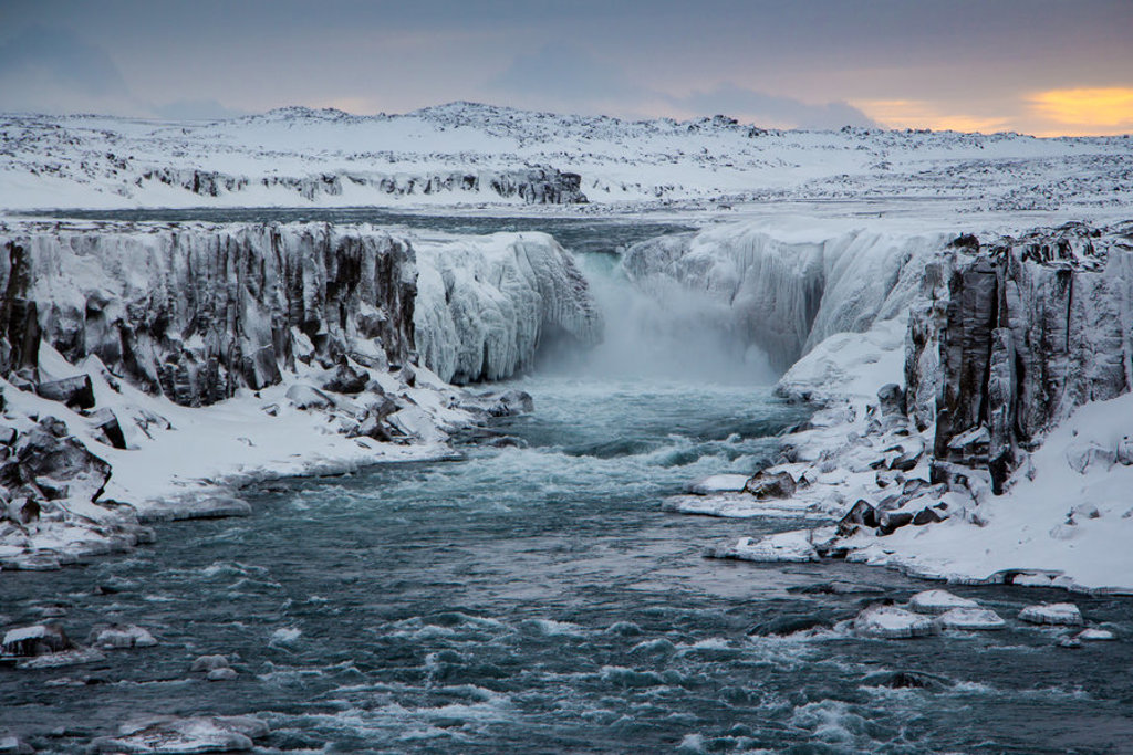 Bevroren waterval en kloof in Noord-IJsland tijdens een groepsrondreis, met besneeuwde rotsen en stromend water.