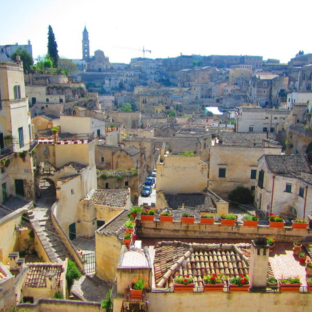 Uitzicht over de historische huizen en daken van Matera, Italië, met kerktoren op de achtergrond.