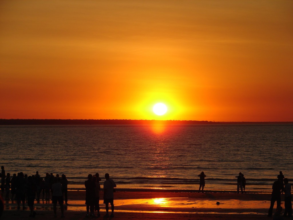 Zonsondergang boven zee bij Darwin met silhouetten van mensen op het strand tijdens een groepsrondreis Australië.