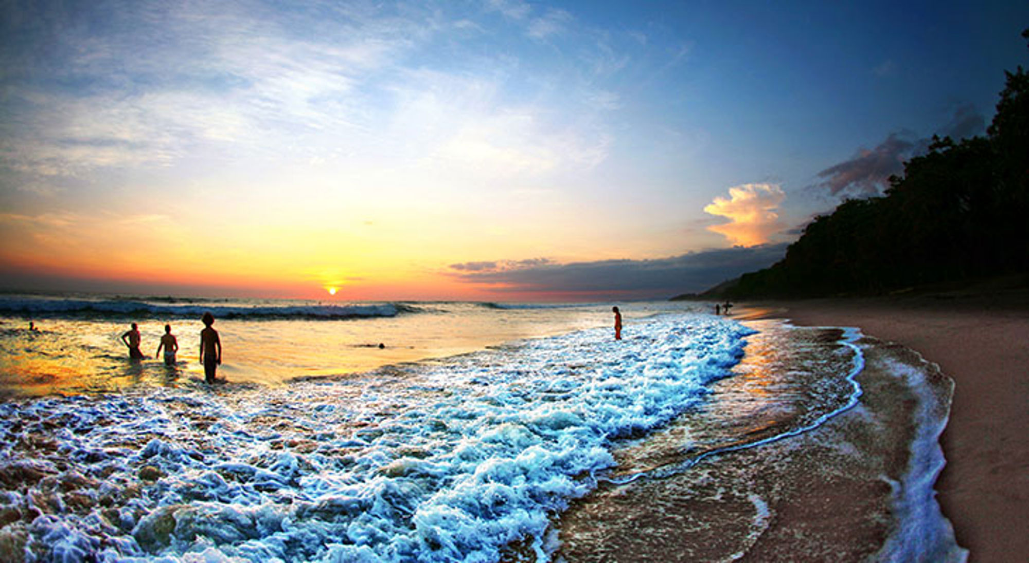 Zonsondergang aan een strand in Costa Rica met golven en mensen in zee.