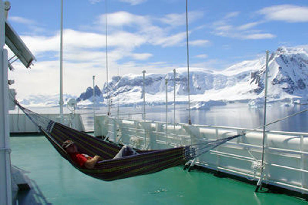 Reiziger in hangmat op het dek van expeditieschip met uitzicht op besneeuwde bergen in Antarctica.