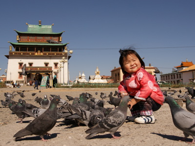 Kind in traditionele Mongoolse kleding tussen duiven op het plein bij het Gandan-klooster in Ulaanbaatar.