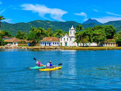 Kajakkers op zee bij Paraty met de witte kerk en groene bergen op de achtergrond, Route Buenos Aires naar Rio.