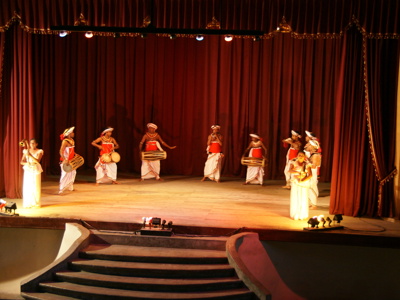 Traditionele Sri Lankaanse dans- en drumvoorstelling op een podium met rode gordijnen.