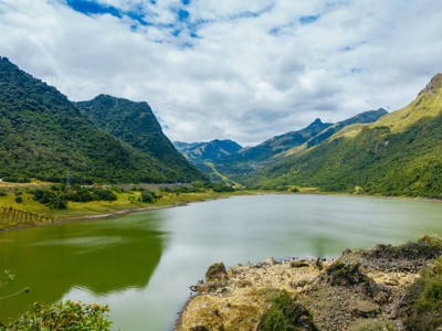 Groen bergmeer in de Andes tijdens de Route Ecuador (22 dagen), omringd door beboste bergen en wolkenlucht.