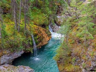 Turquoise rivierkloof met waterval in een dennenbos langs de Route Canada.