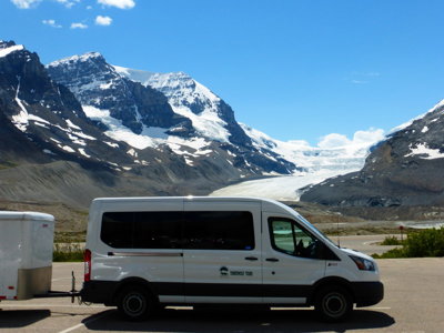 Witte bus in Canada met besneeuwde bergen en gletsjer op de achtergrond.