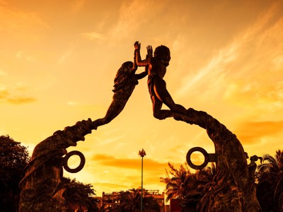 Standbeeld van twee figuren die elkaar aanraken op een boog, bij zonsondergang op Route Ruta Maya.