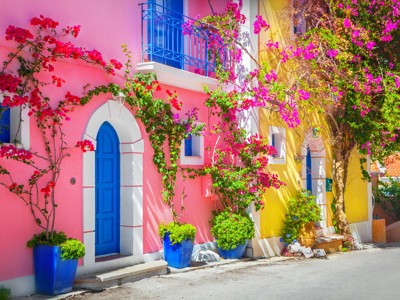 Kleurrijke straat in Griekenland met roze en gele huizen, blauwe deuren en bougainvillea in bloei.