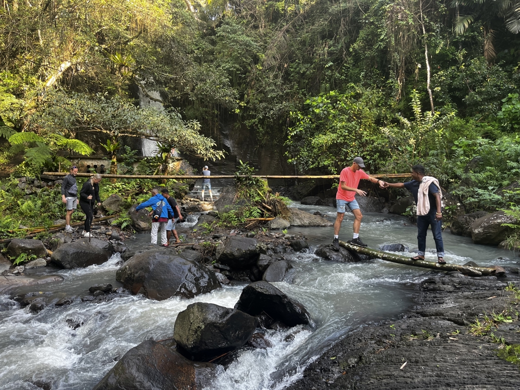 Gezin steekt een rivier over via een boomstambrug tijdens familiereis Kleine Sunda Eilanden, Indonesië.