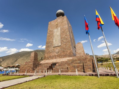 Monument Mitad del Mundo bij de evenaar in Ecuador, met vlaggen en berglandschap op de achtergrond.