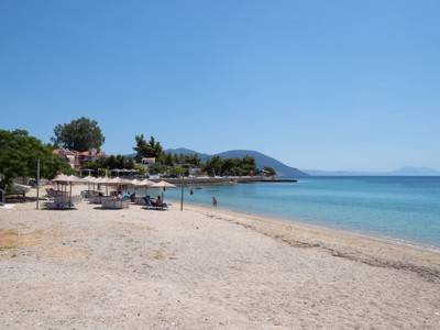 Zandstrand op Evia met parasols en ligbedden aan helderblauw water, met bergen op de achtergrond.