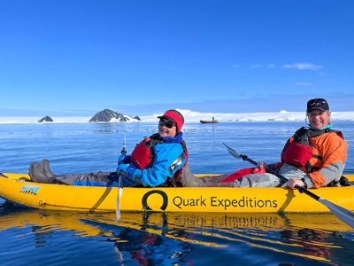 Twee reizigers kajakken op zee bij Antarctica, met ijs en bergen op de achtergrond.