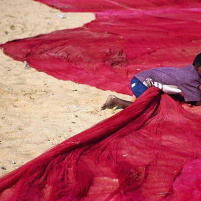 Jongen op het strand tussen rode visnetten tijdens een rondreis langs de hoogtepunten van Zuid-India.