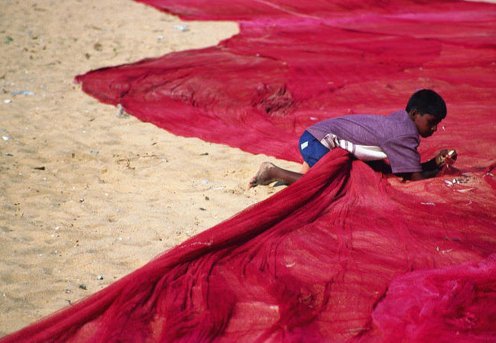Jongen op het strand tussen rode visnetten tijdens een rondreis langs de hoogtepunten van Zuid-India.
