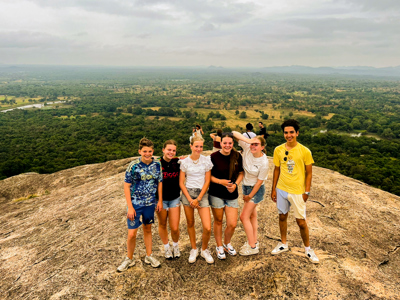 Groep jongeren op een rots met panoramisch uitzicht over het groene landschap van Sri Lanka.