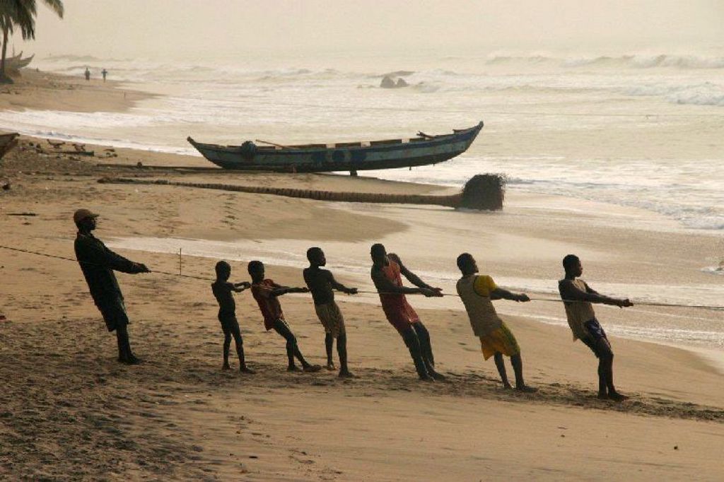 Vissers trekken een boot aan land op het strand tijdens de groepsrondreis Ghana, Togo en Benin.