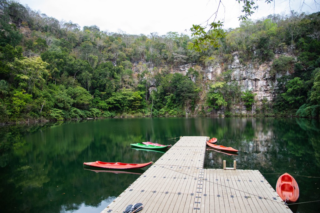 Kajaks bij een steiger op een groene lagune, omringd door jungle en rotswanden in Mexico.