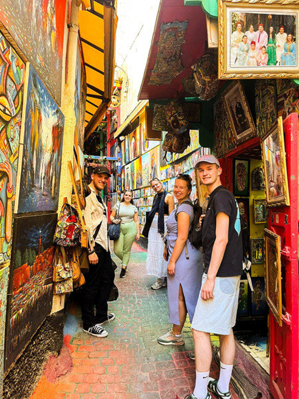 Jonge reisgroep in een smalle, kleurrijke soukstraat met kunst en souvenirs tijdens 22-35ers reis Marokko.