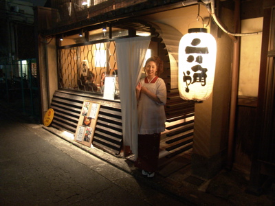 Traditionele izakaya in Japan met papieren lantaarn en gastvrouw bij de ingang in de avond.