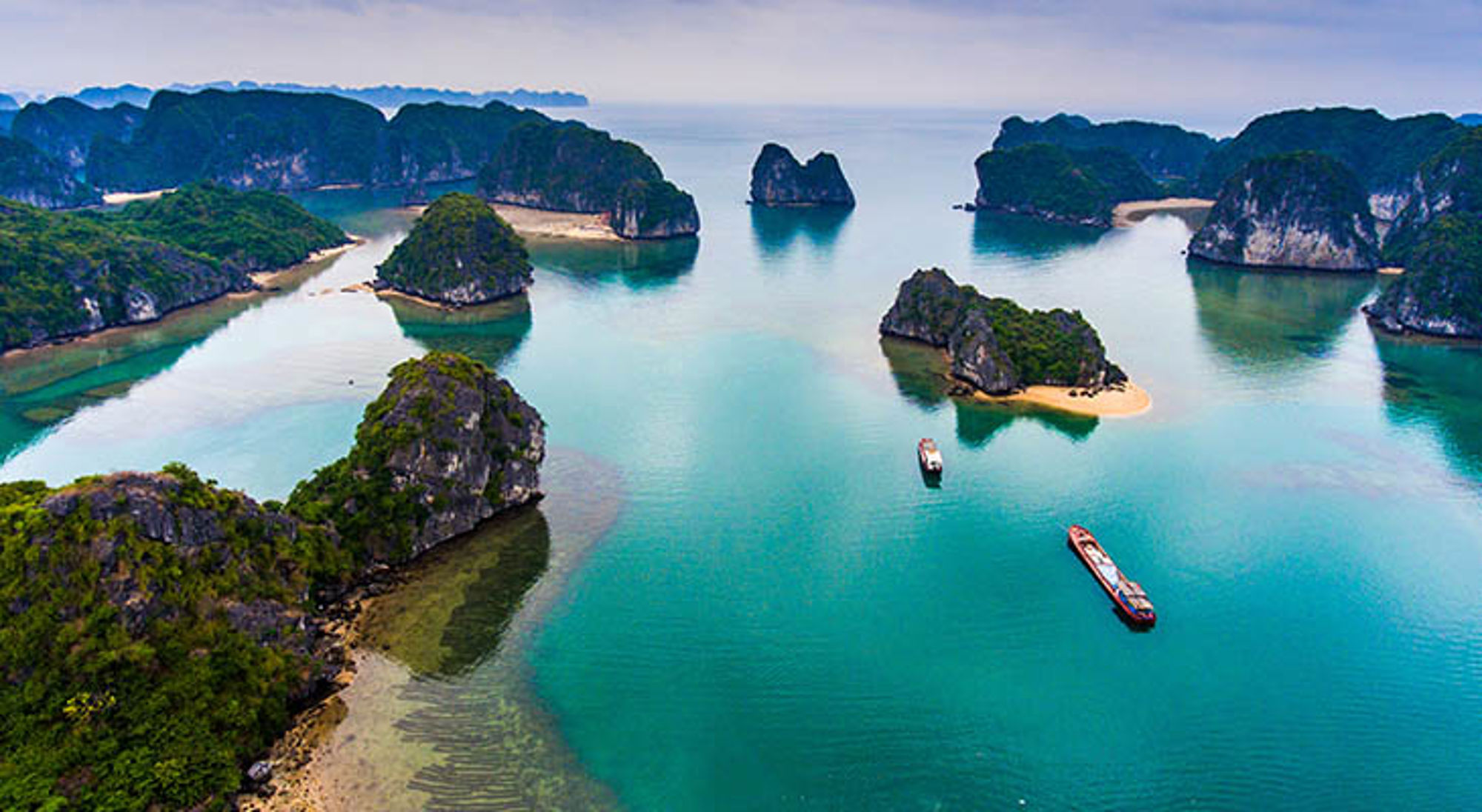 Karst-eilanden en turquoise water in Halong Bay, Vietnam, met boten tussen de rotsformaties.