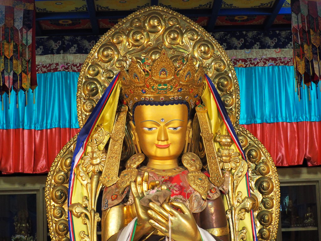 Groot gouden boeddhabeeld met kroon en kleurrijke doeken in een tempel in Japan.