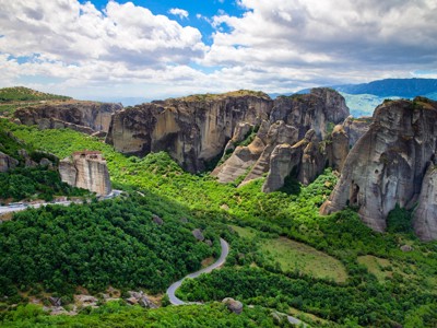 Uitzicht op de rotsformaties en kloosters van Meteora in Noord-Griekenland, met groene valleien en slingerweg.