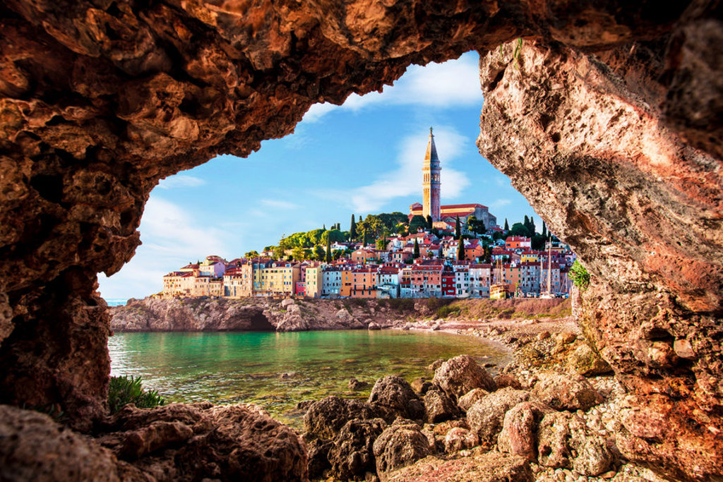 Uitzicht vanuit een rotsgrot op de kleurrijke kustplaats Rovinj in Istrië, ideaal als stop tijdens een fietsvakantie.