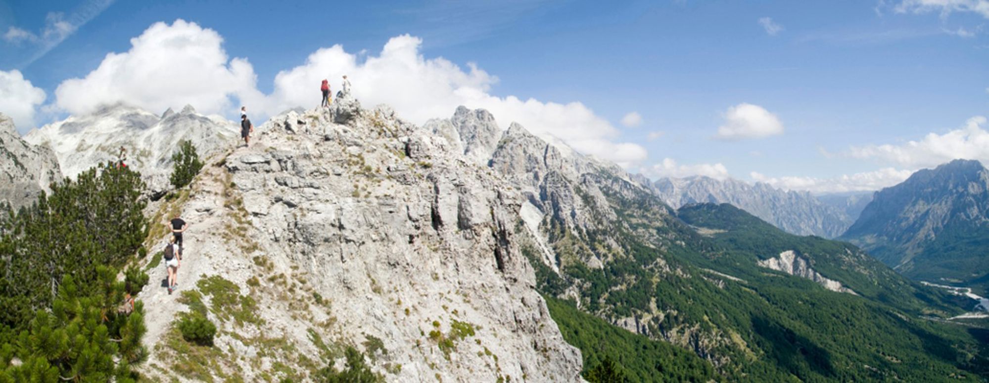 Wandelaars op een bergkam met uitzicht op de Albanese Alpen onder een blauwe lucht.