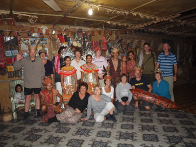 Groepsfoto met reizigers en lokale bewoners in traditionele kleding in een longhouse op Maleisisch Borneo.