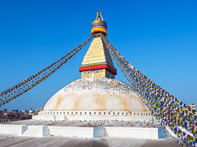 Boudhanath-stoepa in Kathmandu met kleurrijke gebedsvlaggen onder een heldere blauwe lucht.