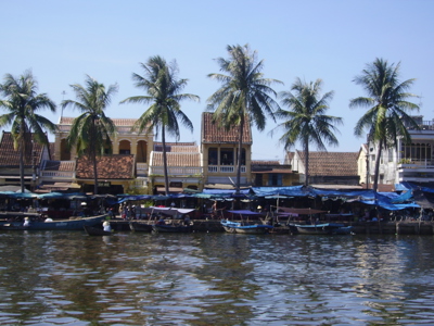 Drijvende markt met boten aan de rivier, palmbomen en huizen langs de oever in Vietnam.