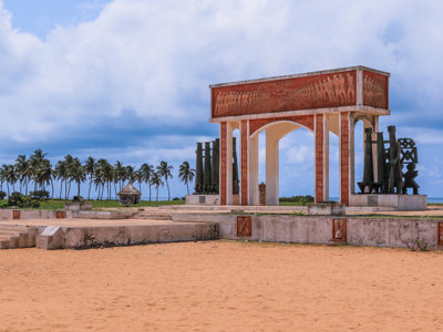 Monument Independence Arch op het strand van Lomé, Togo, met palmbomen en zee op de achtergrond.