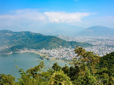 Uitzicht over Pokhara en het Phewa-meer, met groene heuvels en bergen op de achtergrond.