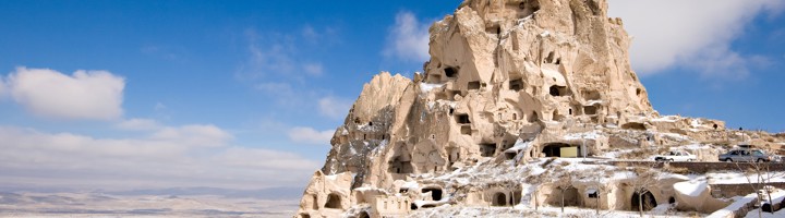 Uchisar Castle in Cappadocië, uitgehouwen in tufsteen en bedekt met sneeuw onder een blauwe lucht.