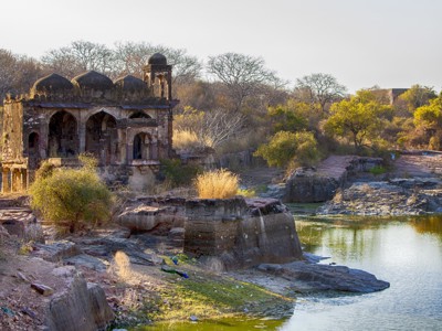 Historisch paviljoen met koepels aan een rivier in Noord-India, omringd door rotsen en struiken.