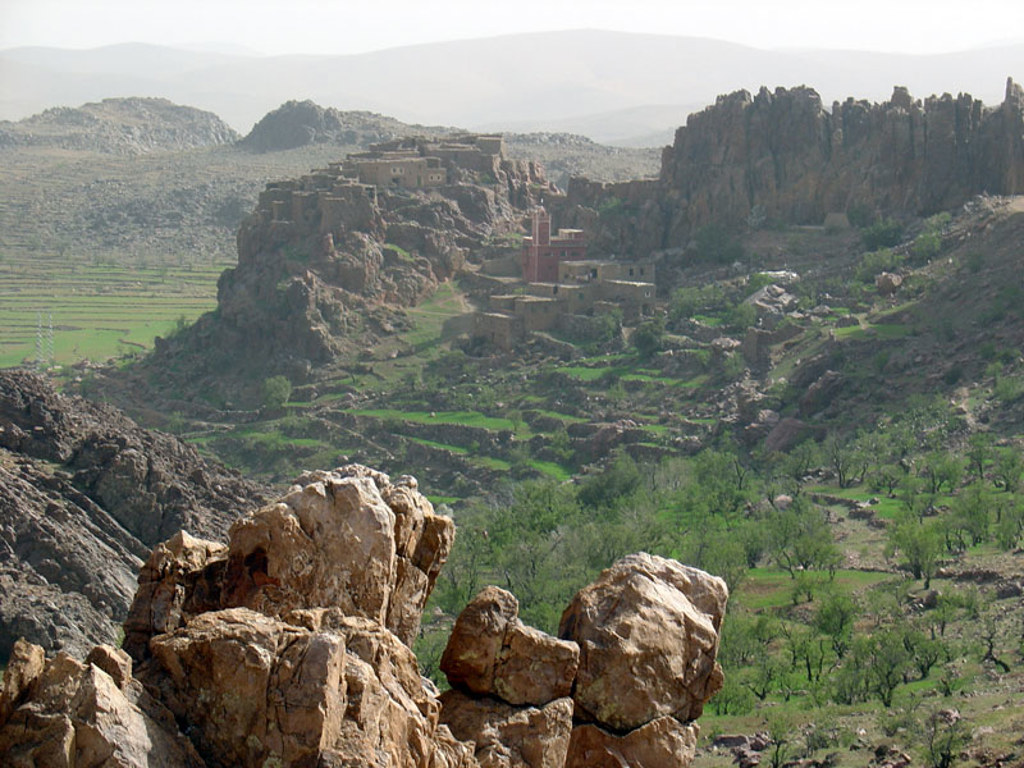 Uitzicht op bergdorp met moskee tussen rotsen en groene terrassen in Marokko.