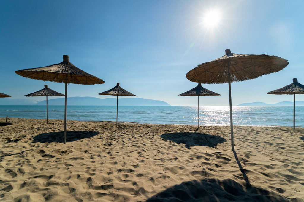 Rieten parasols op een zandstrand aan zee in Albanië, met zon en uitzicht op de kustlijn.