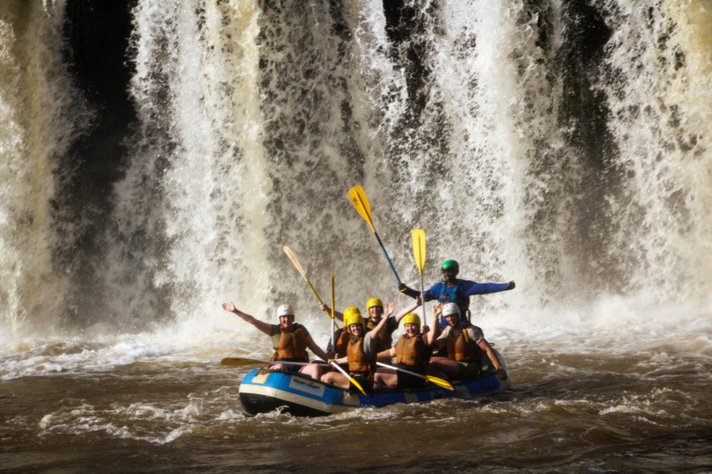 Groep 22-35ers tijdens raften op wildwater met waterval in Kenia of Tanzania.