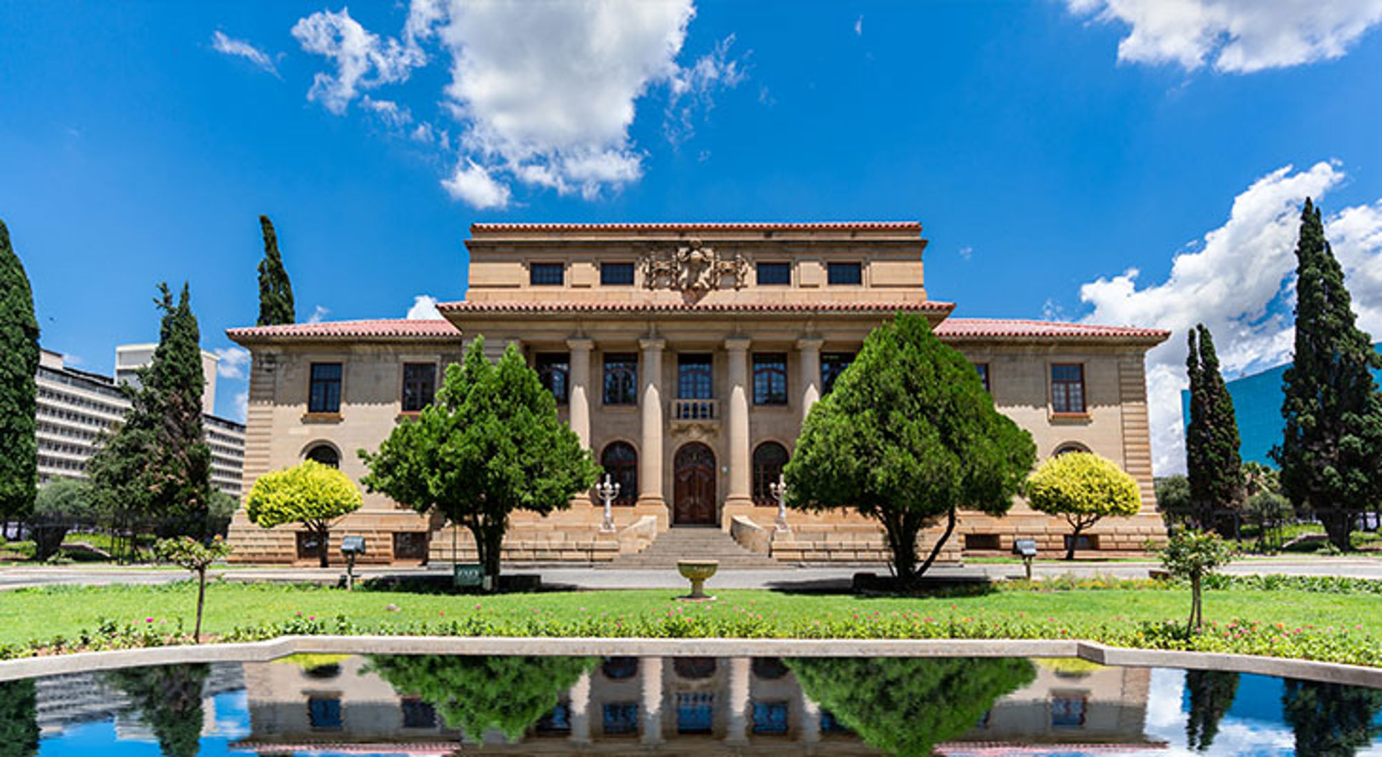 Union Buildings in Pretoria, Zuid-Afrika, met reflectievijver en tuinen onder een blauwe lucht.